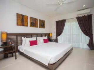 Nowoczesna sypialnia idealna na relaks po kite camp; wygodne łóżko, jasny pościel, czerwone poduszki, światło dzienne.