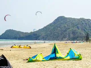 Kolorowe latawce na plaży KiteAway, uczestnicy wyjazdu kitesurfingowego spacerują brzegiem wśród zielonych wzgórz i latawców.