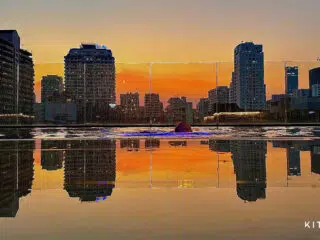 Osoba pływa w basenie na dachu o zachodzie, na tle miasta. Klimatyczne wakacje z kitesurfingiem KiteAway. Logo KITEAWAY w rogu.