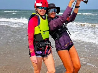 Dwie kobiety na plaży w sprzęcie do kitesurfingu i kaskach podczas kite camp KiteAway. Idealny klimat na wyjazdy kitesurfingowe.