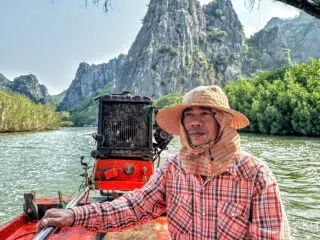 Mężczyzna w koszuli w kratę i kapeluszu płynie czerwoną łodzią przez mangrowce i góry, w trakcie wyjazdu kitesurfingowego z KiteAway.