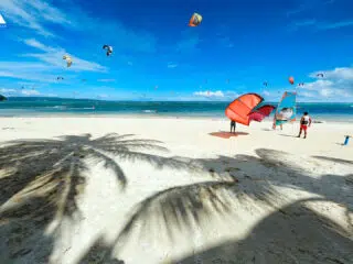 Kitesurfingowcy szykują sprzęt na słonecznej plaży KiteAway; kolorowe latawce, biały piasek, idealne wyjazdy kitesurfingowe.