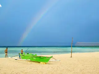 Dwie osoby przy zielonej łodzi na plaży, turkusowa woda, tęcza-idealny dzień na wyjazdy kitesurfingowe z KiteAway.