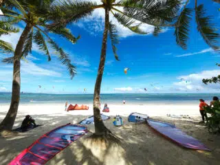 Plaża z palmami, latające latawce, kurs kitesurfingu i wyjazdy kitesurfingowe z KiteAway pod błękitnym niebem.