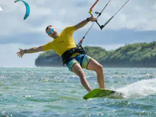 Uśmiechnięty kitesurfer na oceanie podczas kite campu KiteAway; w tle wyspa i inny rider. Idealne wyjazdy kitesurfingowe!.