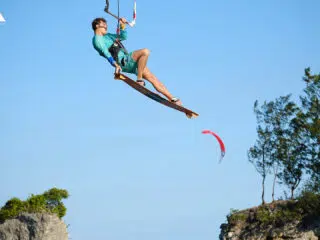 Kitesurfer w turkusowym stroju unosi się nad wodą podczas wyjazdu KiteAway, to klify, drzewa i latawce - wakacje z kitesurfingiem.