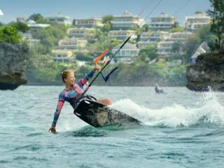 Kitesurfer w kolorowym piance sunie po turkusowej wodzie przy skałach-wyjazdy kitesurfingowe z KiteAway pełne emocji!.