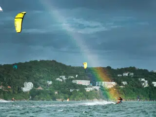 Kurs kitesurfingu KiteAway: nauka na oceanie przy zielonym wzgórzu, tęcza nad wodą i białe budynki - wyjazdy kitesurfingowe.