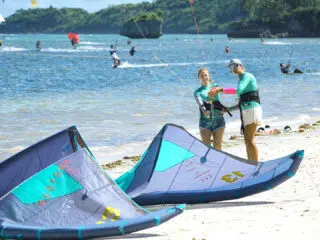 Dwie osoby szykują sprzęt na plaży podczas wyjazdu kitesurfingowego z KiteAway; kolorowe latawce, kite camp nad morzem.