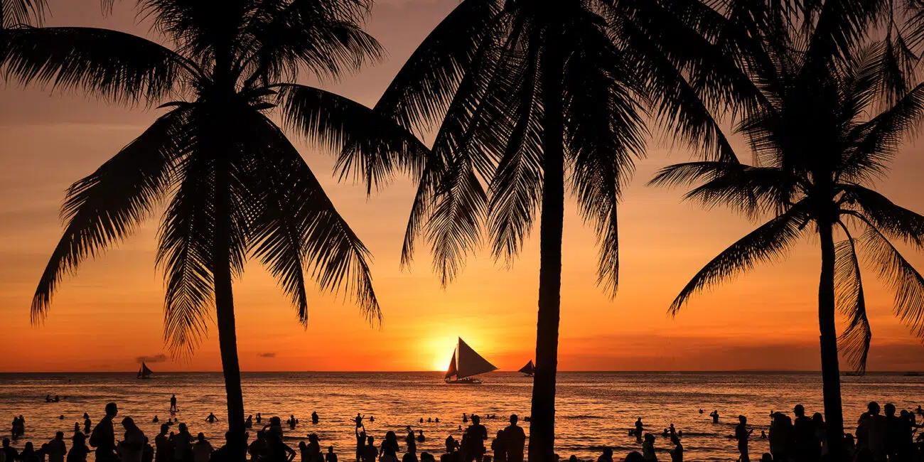 Plaża o zachodzie słońca, sylwetki palm i łódek; idealne miejsce na wyjazdy kitesurfingowe z KiteAway.