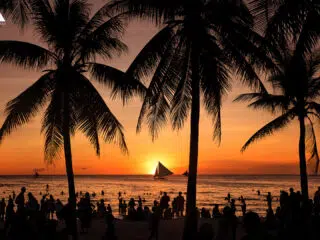 Plaża o zachodzie słońca, sylwetki palm i łódek; idealne miejsce na wyjazdy kitesurfingowe z KiteAway.