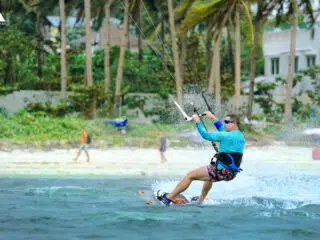 Kitesurfer w okularach i niebieskiej koszulce pływającej przy palmowej plaży - wyjazdy kitesurfingowe z KiteAway, idealne kite trip.