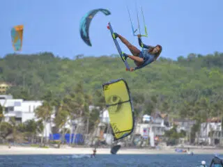 Kitesurfer w powietrzu na tle kolorowych latawców; atmosfera kite camp KiteAway - idealne wakacje z kitesurfingiem.
