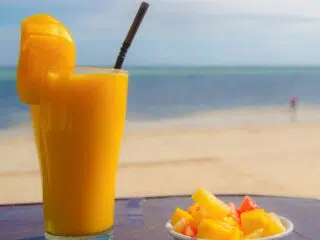 Szklanka soku mango i owoce na plażowym stole - idealne orzeźwienie po kursie kitesurfingu z KiteAway na kite campie.