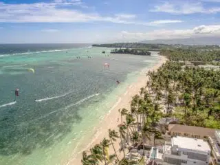 Plaża z palmami, turkusowa woda, osoby na latawcach - wyjazdy kitesurfingowe KiteAway, wakacje z kitesurfingiem.