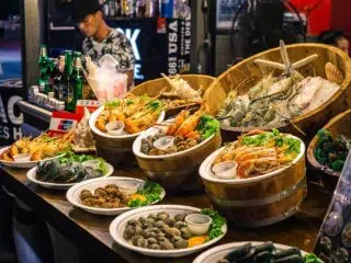 Kolorowe stoisko z owocami morza na kite campie KiteAway - idealne wakacje z kitesurfingiem; w tle napoje i obsługa.