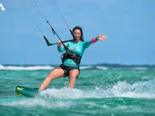 Kitesurfer na turkusowej wodzie podczas kite tripu z KiteAway, w uprzęży, z latawcem na tle fal i błękitnego nieba.