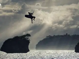 Sylwetka kitesurfera w miejscowości nad wodą, promienie słońca i skały-idealne na wyjazdy kitesurfingowe z KiteAway.pl.