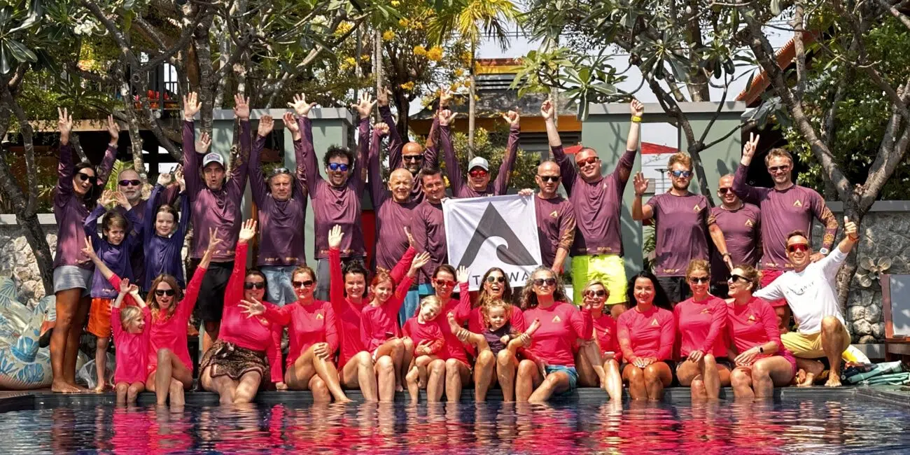 Uczestnicy wyjazdu kitesurfingowego KiteAway w kolorowych koszulkach świętują przy basenie pod banerem "kite camp".