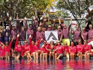 Uczestnicy wyjazdu kitesurfingowego KiteAway w kolorowych koszulkach świętują przy basenie pod banerem "kite camp".