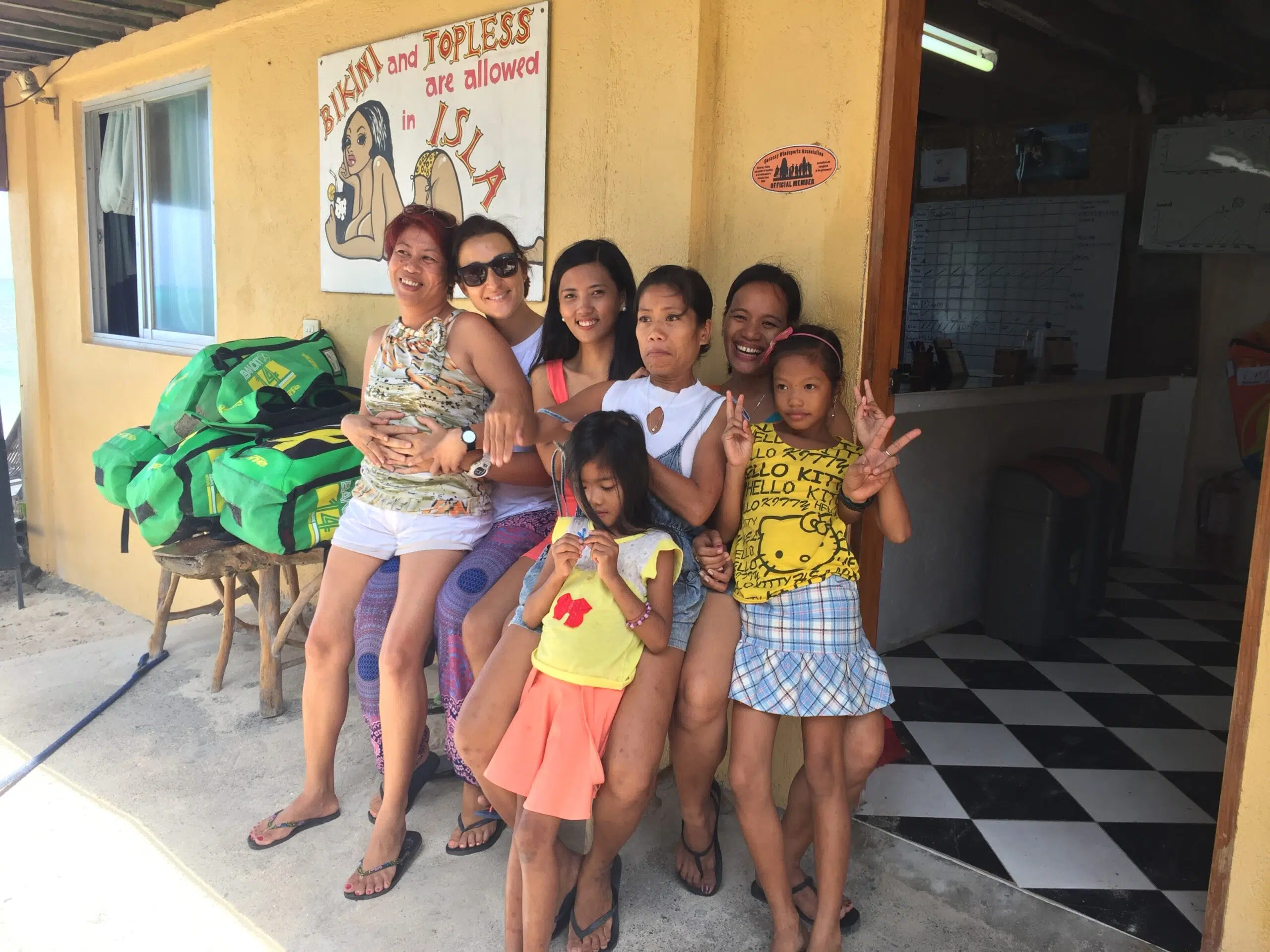 Sześć kobiet i dwie dziewczynki uśmiechają się przed budynkiem na wakacjach z kitesurfingiem z KiteAway - idealnym kite campem.