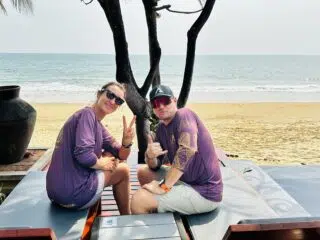 Dwie osoby w fioletowych koszulkach odpoczywają na leżakach przy plaży KiteAway, promując wakacje z kitesurfingiem i kite camp.