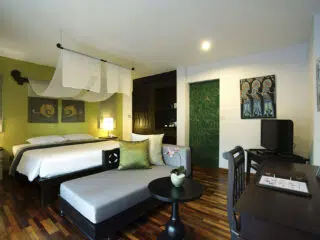 Nowoczesny pokój hotelowy KiteAway idealny na wyjazdy kitesurfingowe: łóżko, sofa, biurko, zielona ściana, drewniana podłoga.