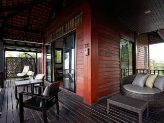 Przytulny, drewniany balkon z sofą i stołem - idealny relaks po wyjeździe kitesurfingowym z KiteAway; widok na zieleń.