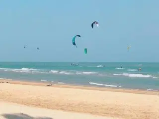 Plaża z jasnym piaskiem, kitesurferzy na lazurowym morzu, kolorowe latawce-idealny spot na wyjazdy kitesurfingowe KiteAway.