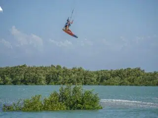Kitesurfer szybujący nad turkusową wodą i zielonymi mangrowcami na tle błękitnego nieba - idealne wyjazdy kitesurfingowe z KiteAway.