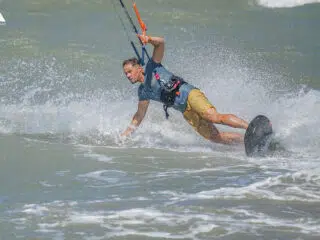Mężczyzna w szarej koszulce i żółtych szortach kitesurfuje na morzu - idealny przykład wyjazdu kitesurfingowego z KiteAway.