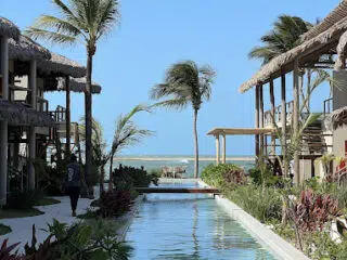 Wąski basen w tropikalnym ogrodzie prowadzi na plażę idealną na wyjazdy kitesurfingowe z KiteAway; osoba idzie przy basenie.