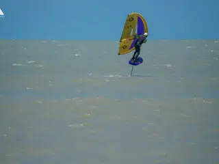 Kitesurfer na hydrofoilu z żółto-fioletowym skrzydłem podczas wakacji z kitesurfingiem KiteAway, idealny kite camp i szkolenie kite.