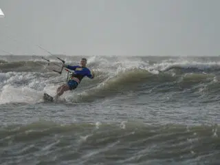 Kitesurfer w niebieskiej koszulce ślizga się po falach podczas wakacji z kitesurfingiem z KiteAway - idealny kite trip.