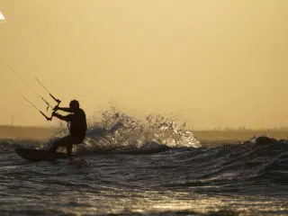 Kitesurfer na tle zachodu słońca podczas wyjazdu kitesurfingowego KiteAway; fale i turbiny w tle, idealny kite spot.
