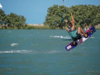 Kitesurfer w trakcie skoku na niebieskiej wodzie podczas wyjazdu KiteAway; słoneczny kite camp, idealne wakacje z kitesurfingiem.