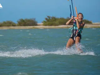 Uśmiechnięta kobieta pływa na kitesurfingu po tureckiej wodzie podczas wyjazdu KiteAway; idealne wakacje z kitesurfingiem.