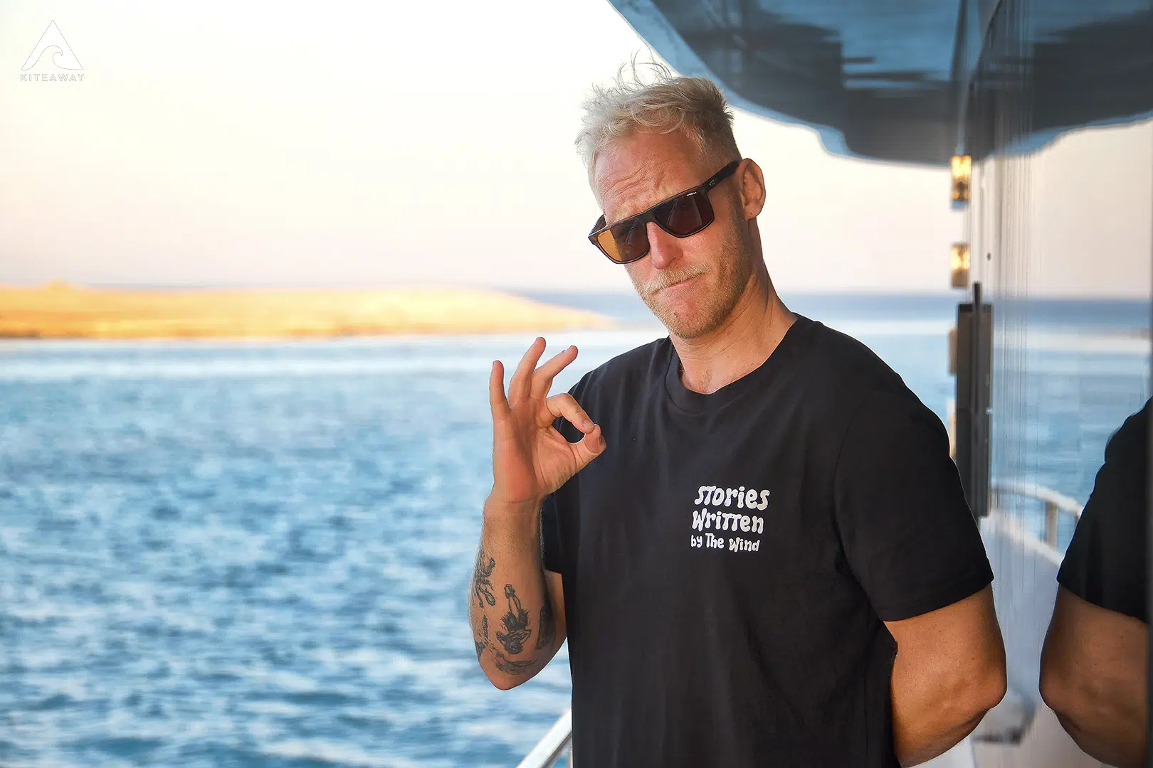 Kobieta z długimi włosami w okularach przeciwsłonecznych i swobodnych ubraniach stoi uśmiechnięta na pokładzie łodzi, gotowa do kitesurfingu w Brazylii. Ocean za nią.