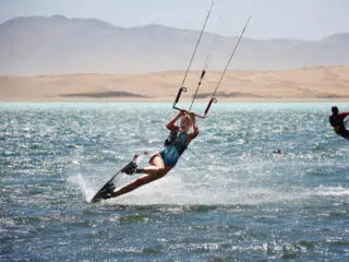 Kitesurfer w kasku i uprzęży pływa na fali, w tle góry - idealny kite camp z KiteAway, wyjazdy kitesurfingowe pełne emocji.