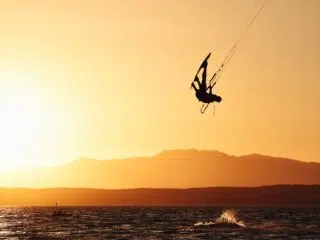 Kitesurfer o zachodzie słońca na tle gór i fal oceanicznych - wyjazdy kitesurfingowe i kite tripy z KiteAway.pl.