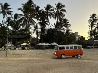 Pomarańczowy van na plaży o zachodzie słońca, palmy i relaksujący się uczestnicy wyjazdu kitesurfingowego z KiteAway.pl.