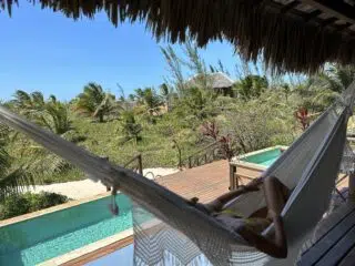 Osoba odpoczywa w hamaku na tarasie z widokiem na basen i zieleń - wymarzone wakacje z kitesurfingiem KiteAway.