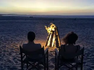 Dwie osoby relaksują się na plaży przy ognisku po dniu pełnym emocji na wyjeździe kitesurfingowym KiteAway, ocean w tle.