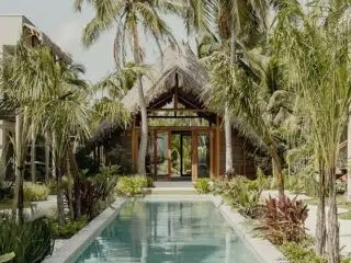 Wąski basen wśród tropikalnych roślin prowadzi do bungalowu - idealne miejsce na relaks po kursie kitesurfingu z KiteAway.