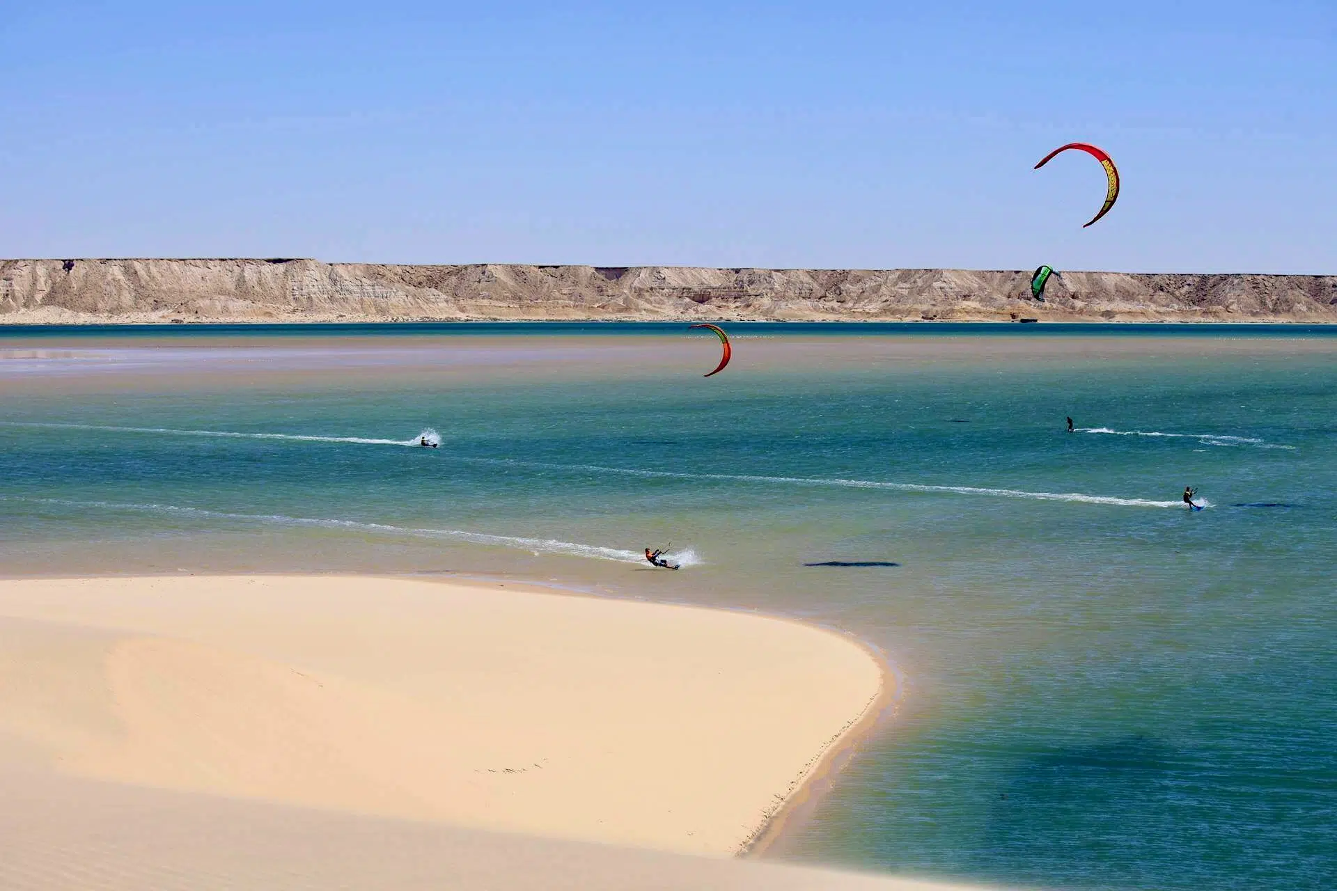 Kitesurferzy ślizgają się po turkusowej wodzie przy pustynnym brzegu - idealny spot na wyjazdy kitesurfingowe z KiteAway.