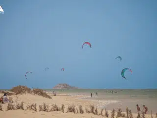 Plaża z kolorowymi latawcami kitesurfingowymi, ludzie odpoczywają - idealny spot na wyjazdy kitesurfingowe z KiteAway.