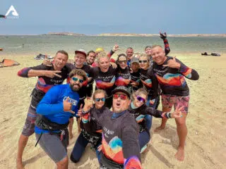 Uśmiechnięta grupa na plaży podczas wyjazdu kitesurfingowego z KiteAway, sprzęt kite w tle, idealny dzień na kite camp.