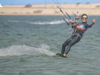 Uśmiechnięty kitesurfer daje kciuk w górę na spocie KiteAway; idealne wakacje z kitesurfingiem, kurs i wyjazdy kitesurfingowe.