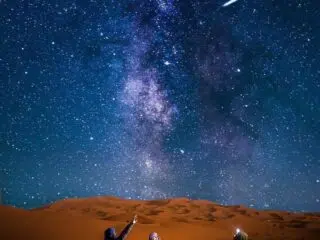 Trzy osoby na krzesłach pod nocnym niebem podczas kite tripu KiteAway, podziwiają Drogę Mleczną na wakacjach z kitesurfingiem.