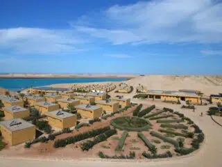 Widok z lotu ptaka na pustynny kurort nad jasnoniebieską wodą, idealny na wyjazdy kitesurfingowe i kite camp KiteAway, pod niebem z chmurami.